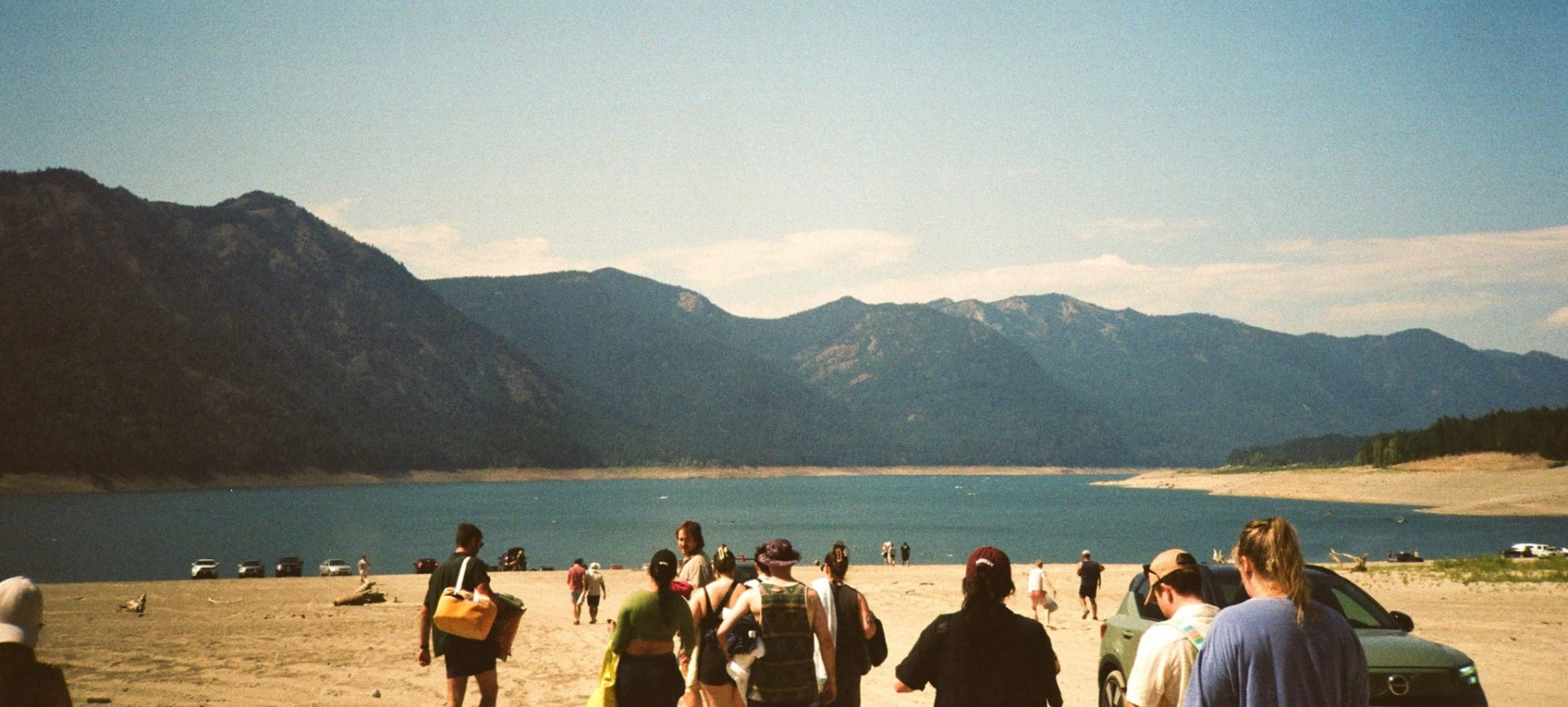 People walking on a sandy beach below mountains and a clear sky